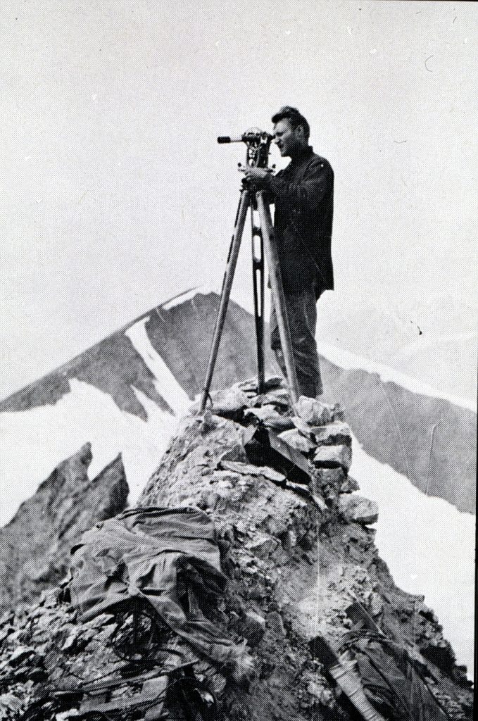 Surveyor looking through transit on top of mountain summit. US Coast and Geodetic Survey personnel.